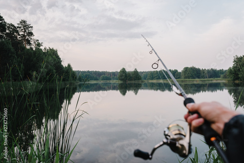 Fisherman with rod, spinning reel on the river bank. Fishing for pike, perch, carp. Fog against the backdrop of lake. background Misty morning. wild nature. The concept of a rural getaway.