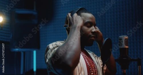 African American young stylish guy rapper taking on headphones and starting to record a song in the dark sound studio. Close up. photo