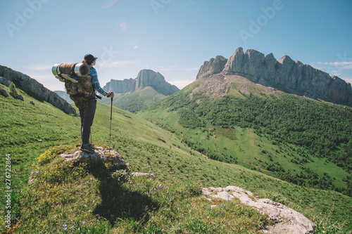 молодая женщина с туристическим рюкзаком смотрит на горную вершину в солнечный летний день