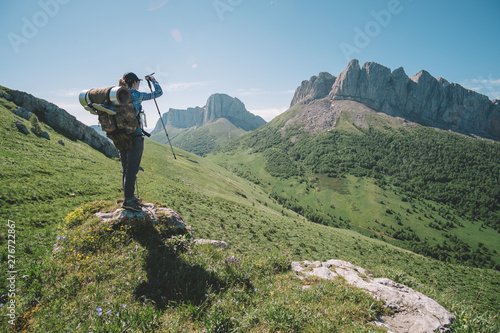 молодая женщина с туристическим рюкзаком смотрит на горную вершину в солнечный летний день