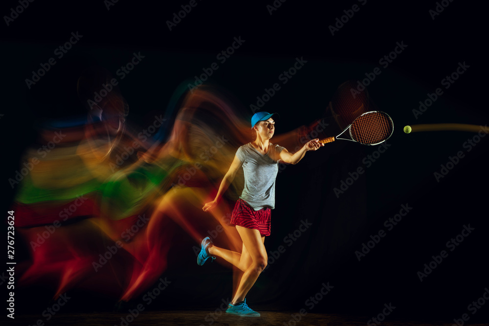 Fototapeta premium One caucasian woman playing tennis isolated on black background in mixed and stobe light. Fit young female player in motion or action during sport game. Concept of movement, sport, healthy lifestyle.