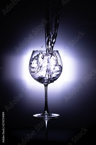 Water pouring into the wine glass on black reflective background, wine glass cup in which fresh water is poured