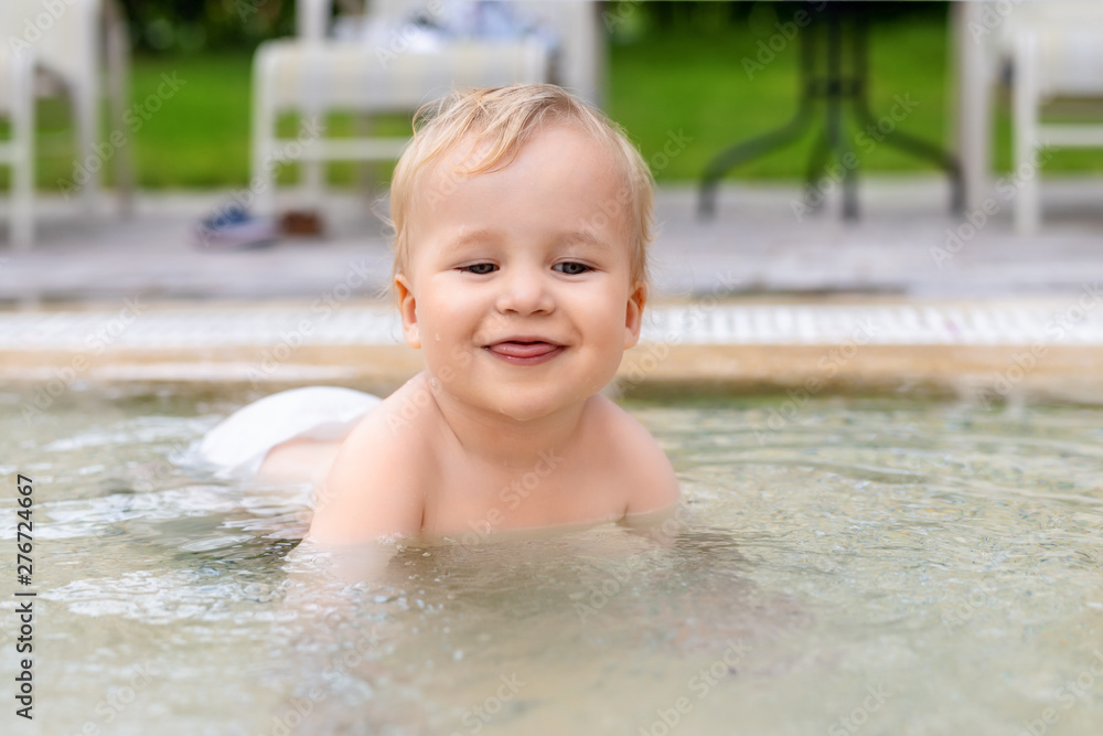 Happy little caucasian blond toddler boy swimming in wading pool on bright summer day at resort. Adorable baby enjoying outdoor water fun activities in shallow water. Children travel and holidays Happy little caucasian blond toddler boy swimming in wading pool on bright summer day at resort. Adorable baby enjoying outdoor water fun activities in shallow water. Children travel and holidays