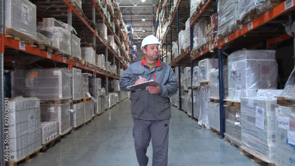 Warehouse worker inspecting high racks with boxes. A man walks in a row, the camera in motion. 4K Slow Mo Warehouse worker inspecting high racks with boxes. A man walks in a row, the camera in motion. 4K Slow Mo