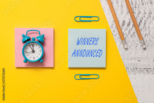 Conceptual hand writing showing Winners Announced. Concept meaning Announcing who won the contest or any competition Notepads colored paper sheet markers alarm clock wooden background photo