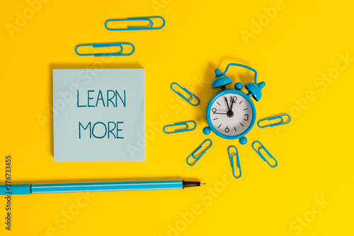 Word writing text Learn More. Business photo showcasing knowledge or skill acquired by instruction Considerable learning Metal alarm clock wakeup clips ballpoint notepad colored background photo