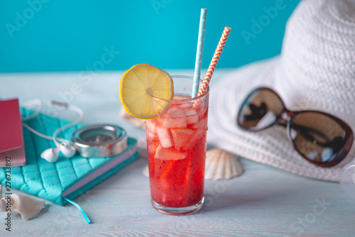 Glass of red lemonade drink with lemon and fruit and straw on the table. Bright summer Sunny holiday in the resort.