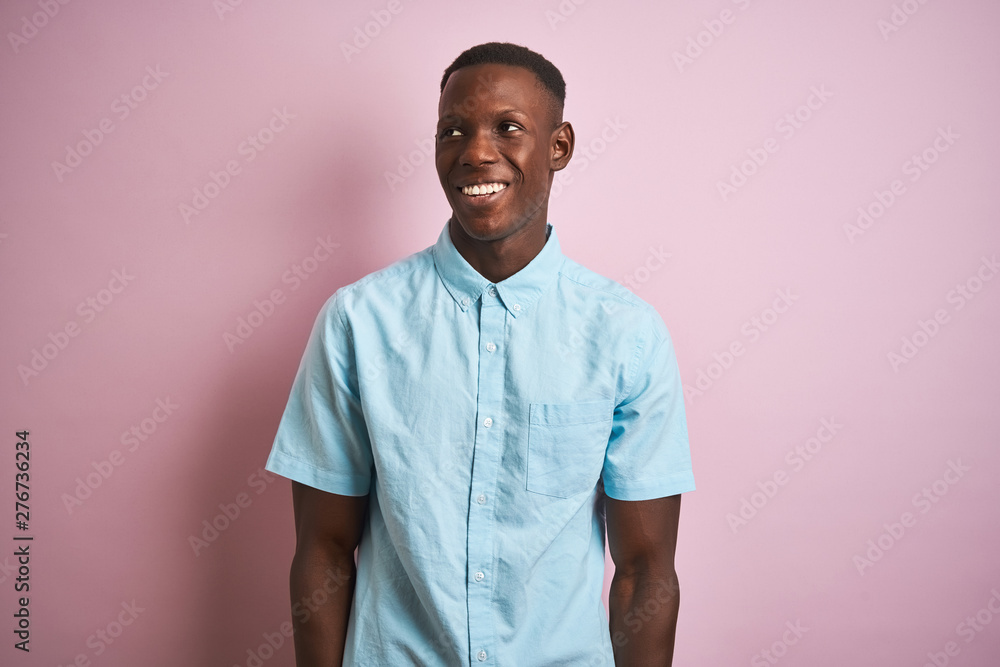 African american man wearing blue casual shirt standing over isolated pink background looking away to side with smile on face, natural expression. Laughing confident. African american man wearing blue casual shirt standing over isolated pink background looking away to side with smile on face, natural expression. Laughing confident.
