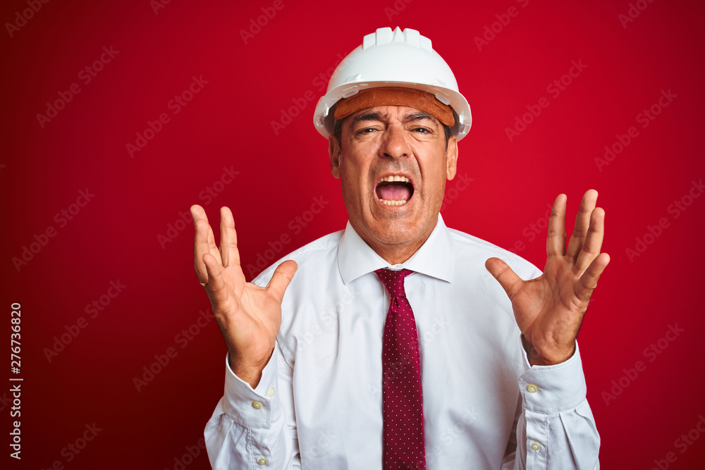 Handsome middle age engineer man wearing security helmet over isolated red background crazy and mad shouting and yelling with aggressive expression and arms raised. Frustration concept. Handsome middle age engineer man wearing security helmet over isolated red background crazy and mad shouting and yelling with aggressive expression and arms raised. Frustration concept.