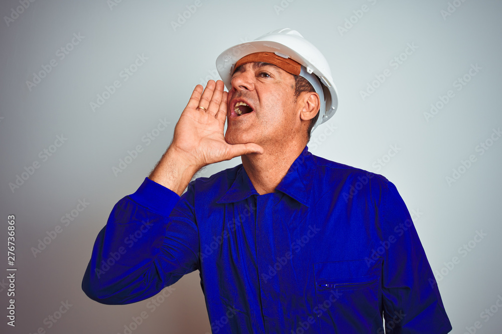 Handsome middle age worker man wearing uniform and helmet over isolated white background shouting and screaming loud to side with hand on mouth. Communication concept.