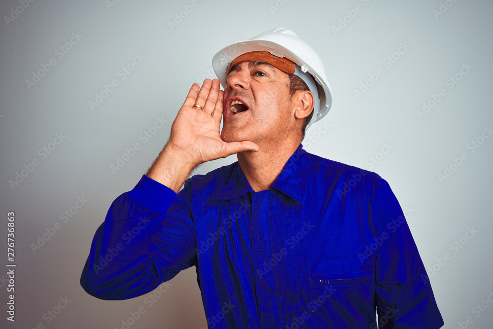 Handsome middle age worker man wearing uniform and helmet over isolated white background shouting and screaming loud to side with hand on mouth. Communication concept. Handsome middle age worker man wearing uniform and helmet over isolated white background shouting and screaming loud to side with hand on mouth. Communication concept.
