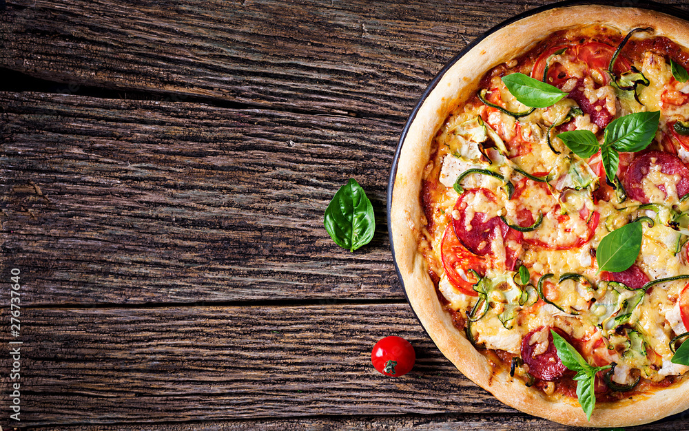 Φωτογραφία Italian pizza with chicken, salami, zucchini, tomatoes and herbs on vintage wooden background
