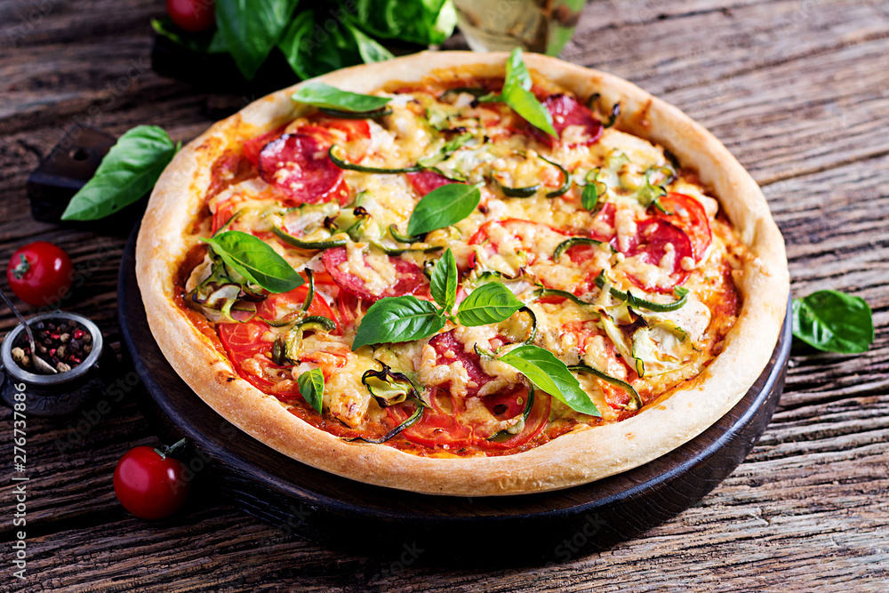 Italian pizza with chicken, salami, zucchini, tomatoes and herbs on vintage wooden background.  Italian cuisine