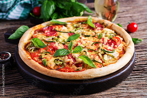 Italian pizza with chicken, salami, zucchini, tomatoes and herbs on vintage wooden background. Italian cuisine