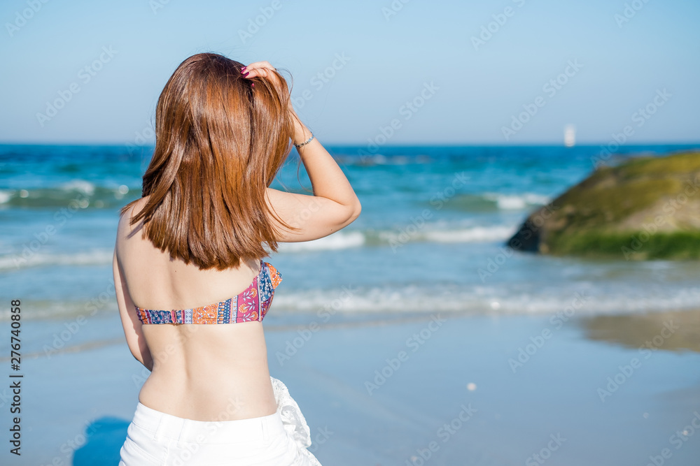 Naklejka premium Young woman sitting on the beach looking at the sea and sky