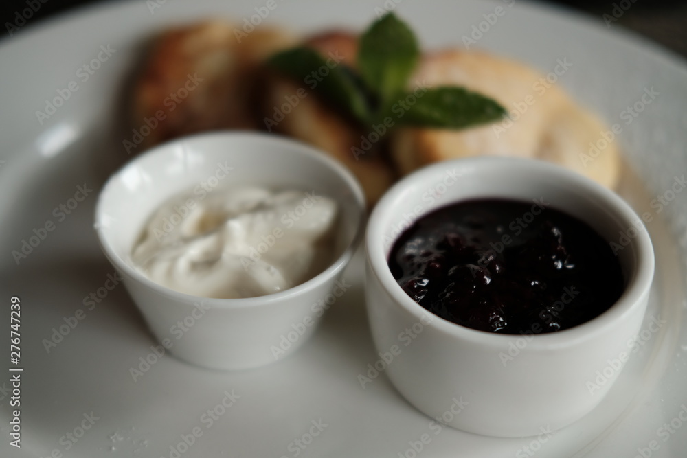 curd cheese cakes and pialas with jam and sour cream on a plate on a table in daylight curd cheese cakes and pialas with jam and sour cream on a plate on a table in daylight