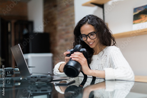 Beautiful woman photographer posing with her camera. The girl work at home with a laptop and a smartphone, wants to do photo processing.