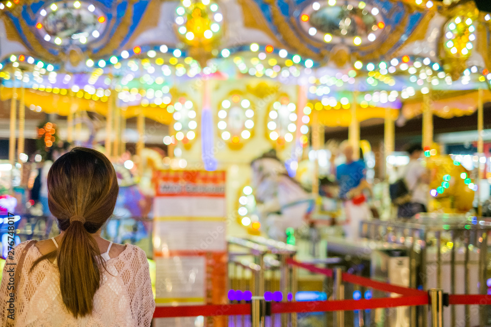 Young woman looking at the amusement park carousel