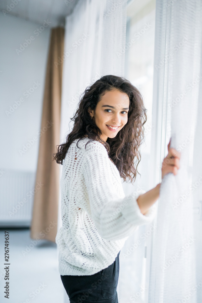 Young woman opening window curtains at home. Young woman opening window curtains at home.