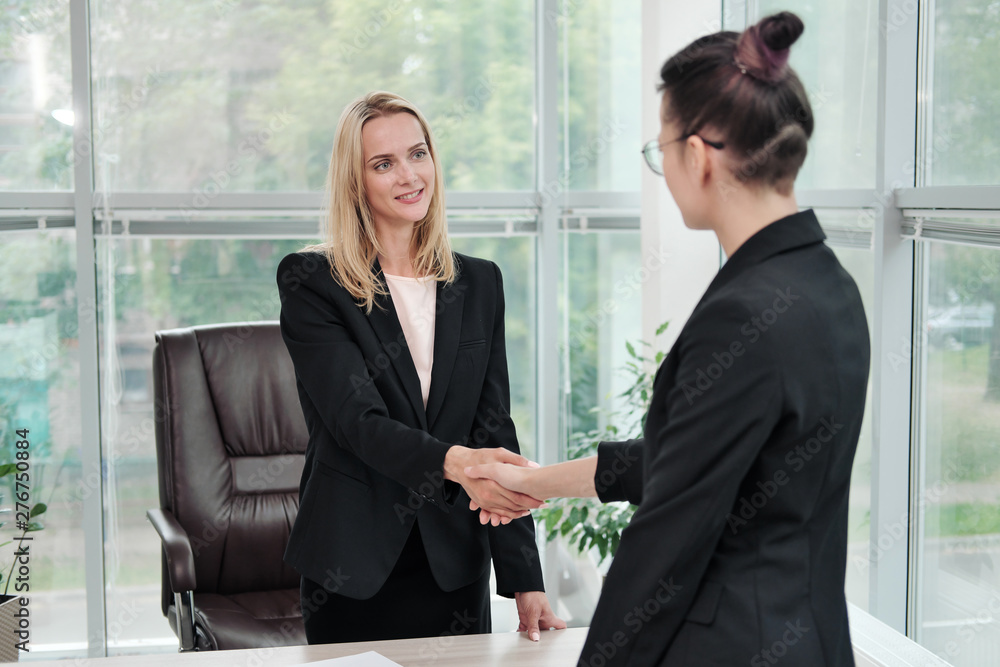 Two beautiful young women in business suits shake hands and smile. Hiring a job. Signing the agreement. Women at work. Two beautiful young women in business suits shake hands and smile. Hiring a job. Signing the agreement. Women at work.