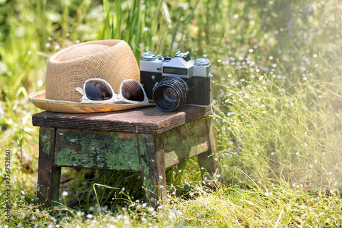 Straw hat, sunglasses and the retro film photo  camera on a wooden chair in the summer garden. Vacation, tourist and travel concept