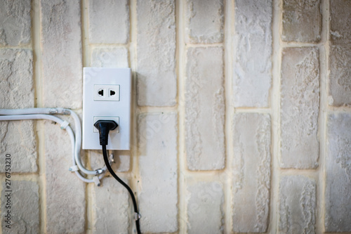 Black power cord cable plugged into wall outlet on white plaster brick wall with copy space. © sommart