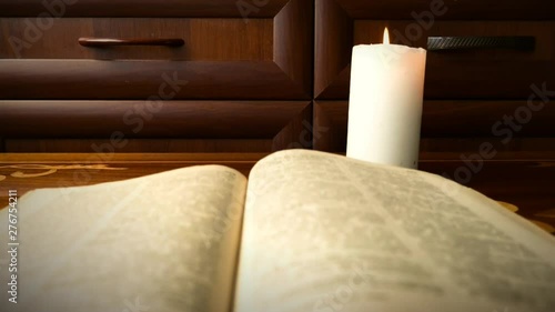 The old book lies on the antique table. The candle burns next to the book on the table.