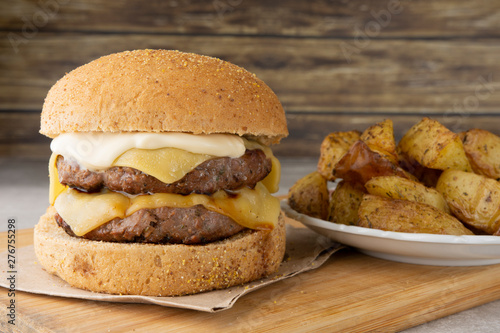 Double cheeseburger over wooden board with roasted potatoes