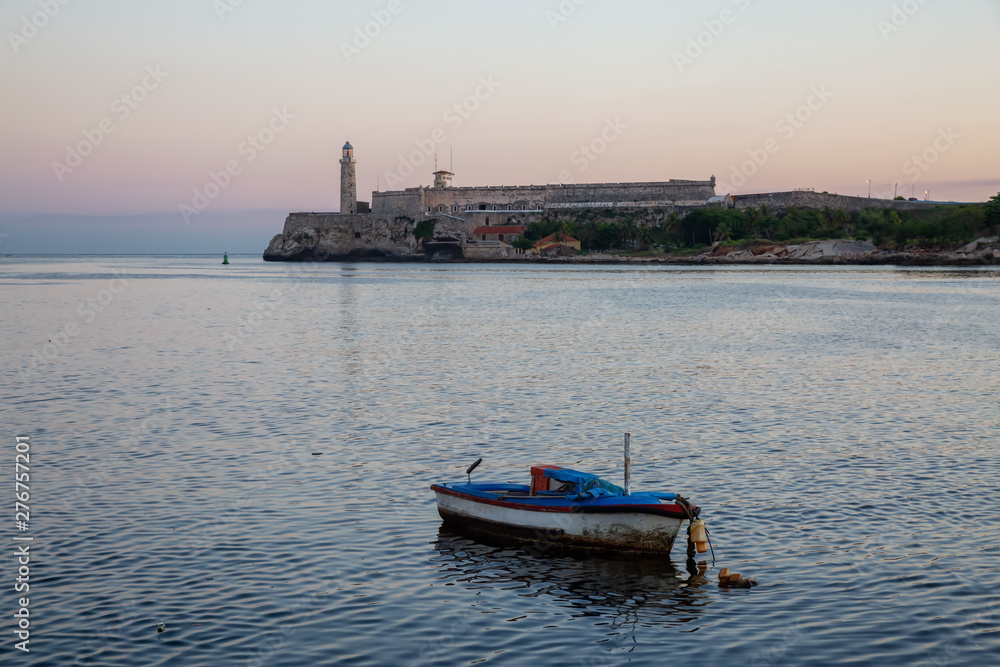 Beautiful view of the small fishing boat with the Lighthouse in the background. Taken in the Old Havana City, Capital of Cuba, during a colorful and sunny sunrise.