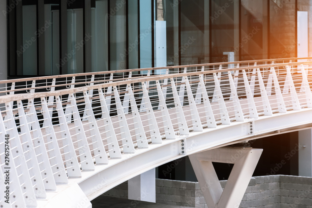 Obraz premium White pedestrian bridge with wooden handrails in the modern area of the city.