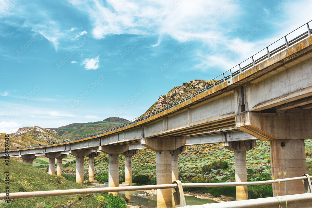 Two road turn highway bridge, viaduct supports in the valley among the green hills, transport infrastructure. Two road turn highway bridge, viaduct supports in the valley among the green hills, transport infrastructure.