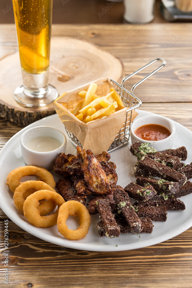 assorted snacks like chicken wings, french fries, rye bread crouton and glass of beer on wooden table assorted snacks like chicken wings, french fries, rye bread crouton and glass of beer on wooden table