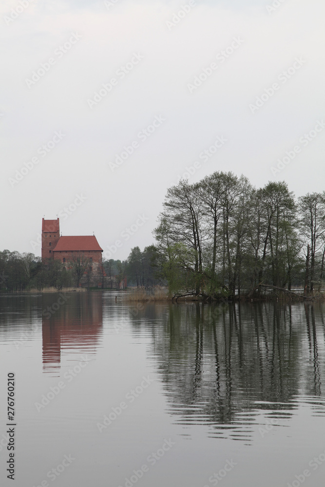 The reflections of the trees and the castle off the lake water on a cloudy day.