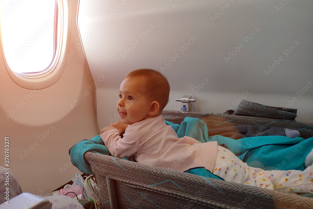 Happy infant baby lyes in special bassinet in airplane at his stomach. First flight of the baby, is impressed and smiles. Traveling with child Stock Photo | Adobe