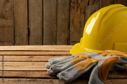 Safety first concept,  personal protective equipment is placed on the wood. Yellow helmet and leather gloves.