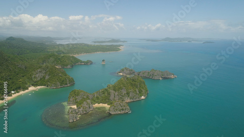 Aerial view of Groups islands with sand beach and turquoise water in blue lagoon among coral reefs, Caramoan Islands, Philippines. Mountains covered with tropical forest.