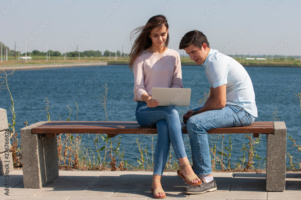 Man and woman using laptop outdoors. Image of young couple man and woman in casual clothes.