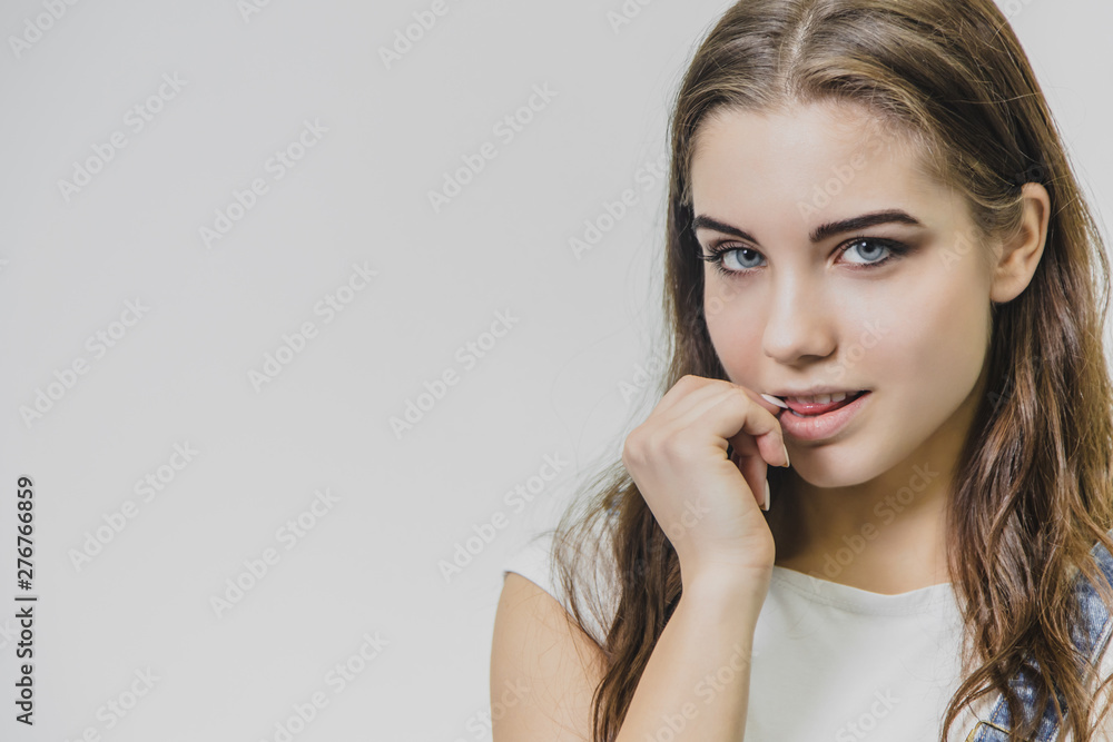 A young beautiful girl stands on a gray background. It is dressed in a denim suit and a white T-shirt. A young beautiful girl stands on a gray background. It is dressed in a denim suit and a white T-shirt.