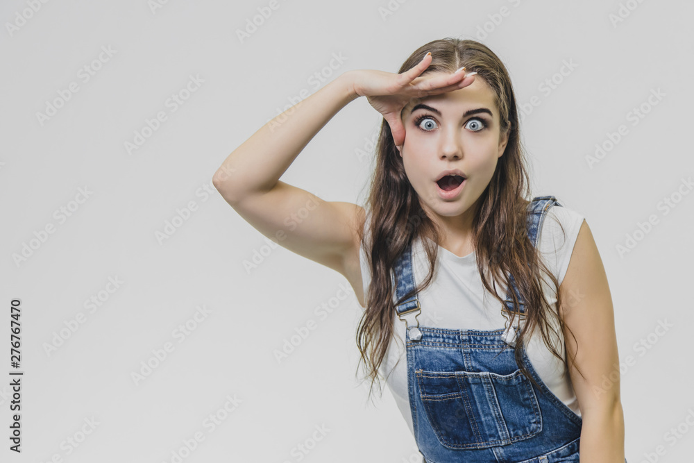 A young beautiful girl stands on a gray background. It is dressed in a denim suit and a white T-shirt. During this time she looks at the camera. A young beautiful girl stands on a gray background. It is dressed in a denim suit and a white T-shirt. During this time she looks at the camera.