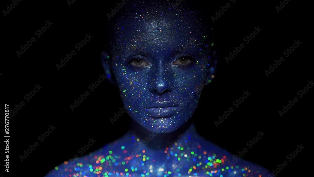 Portrait of beautiful woman with blue sparkles on her face. Girl with art make-up in color Light. Fashion model with colorful makeup Portrait of beautiful woman with blue sparkles on her face. Girl with art make-up in color Light. Fashion model with colorful makeup