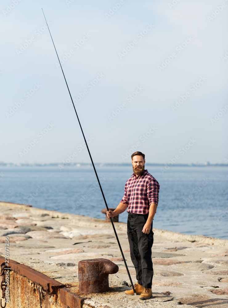 leisure and people concept - bearded fisherman with fishing rod on sea pier