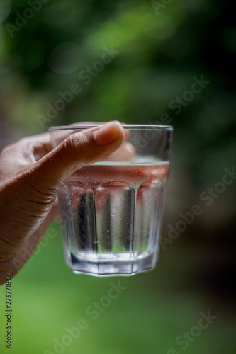 a glass of cold water with drops of water by hand