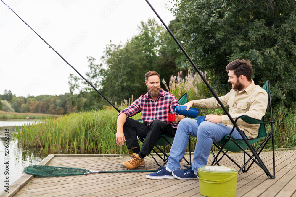leisure and people concept - male friends fishing and drinking tea from thermos leisure and people concept - male friends fishing and drinking tea from thermos