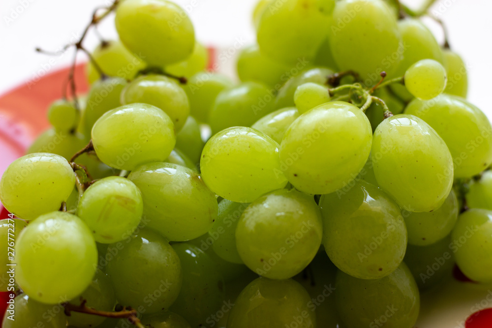 Ripe green grapes in plate on white wooden table, top view. Green grapes in a plate on the table. Green grapes in a red plate on the table. Ripe green grapes in plate on white wooden table, top view. Green grapes in a plate on the table. Green grapes in a red plate on the table.