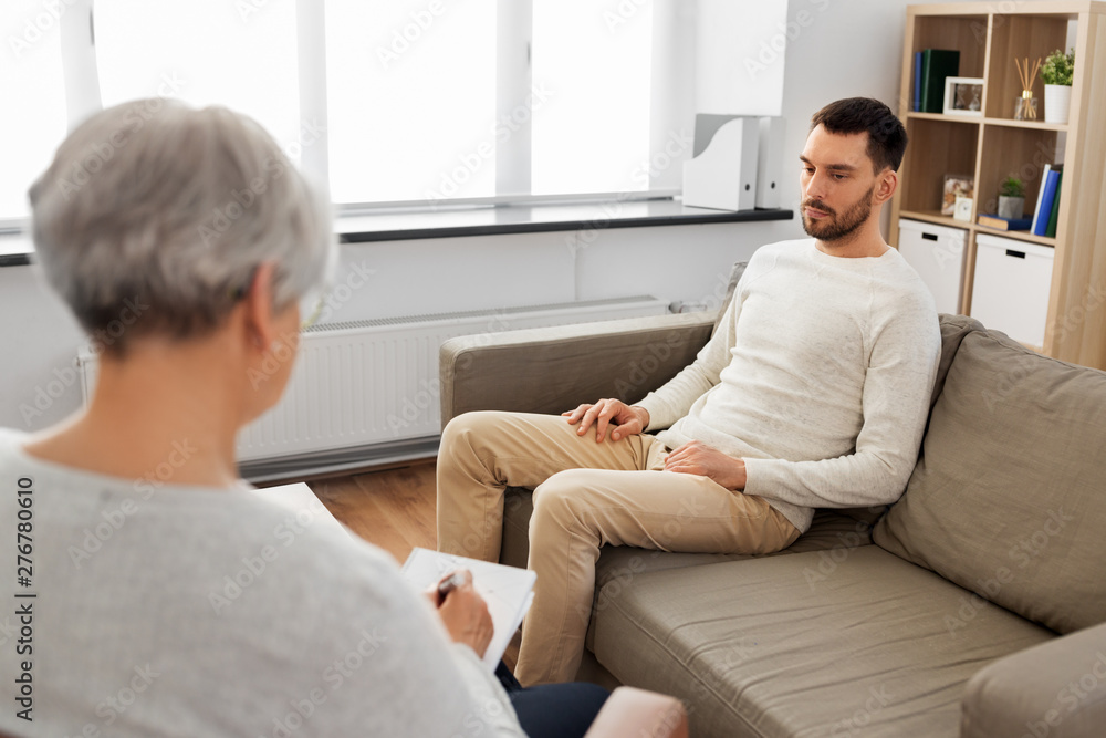 psychology, mental therapy and problem concept - senior woman psychologist taking notes to notebook and sad young man patient at psychotherapy session psychology, mental therapy and problem concept - senior woman psychologist taking notes to notebook and sad young man patient at psychotherapy session