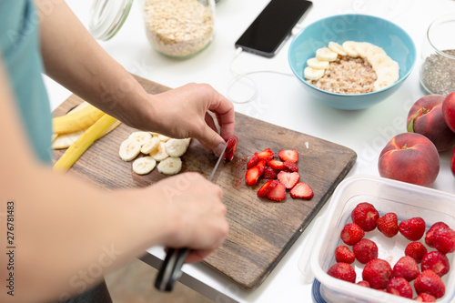 Woman preparing healthy fitness breakfast: oatmeal with bananas, strawberries and chia seeds