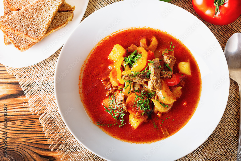 Hot beef hungarian goulash soup with paprika, beef, potatoes, carrots, onion, pepper and herbs. Ingredients for dish. Rustic background. Hot beef hungarian goulash soup with paprika, beef, potatoes, carrots, onion, pepper and herbs. Ingredients for dish. Rustic background.