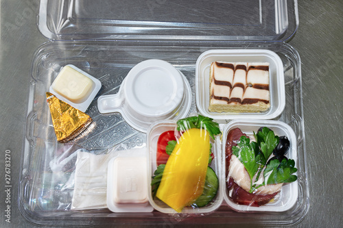 Food served on board of economy class airplane. Plastic lunchbox with food and disposable tableware.