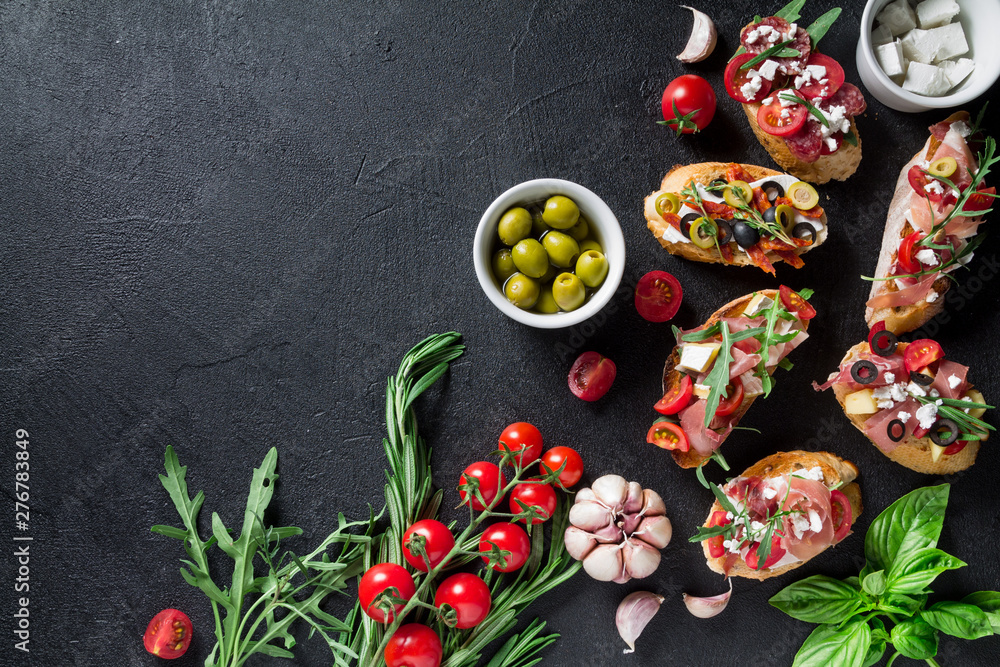 Bruschetta, garlic, olives, tomatoes, a bowl of cheese, rosemary leaves, arugula and basil on a black background. Top view with copy space for your text