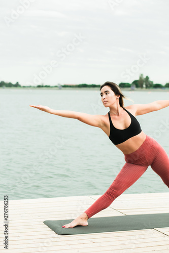 young girl doing yoga outdoors on the pier by the lake.